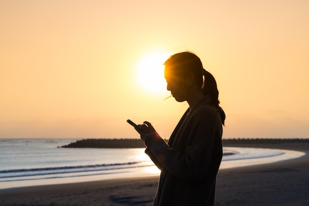 浜辺で日没時に携帯電話を使っている女性のシルエット