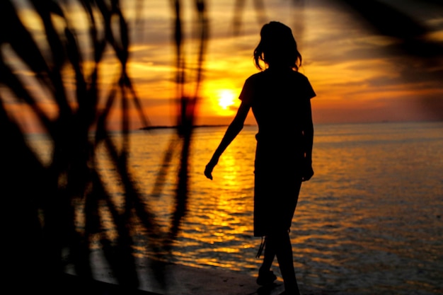 Photo silhouette woman walking at beach during sunset