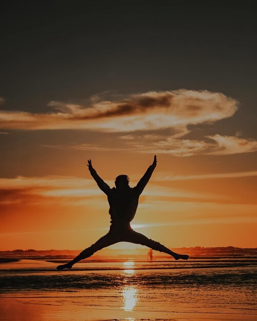 Photo silhouette woman with arms outstretched standing on beach against sky during sunset