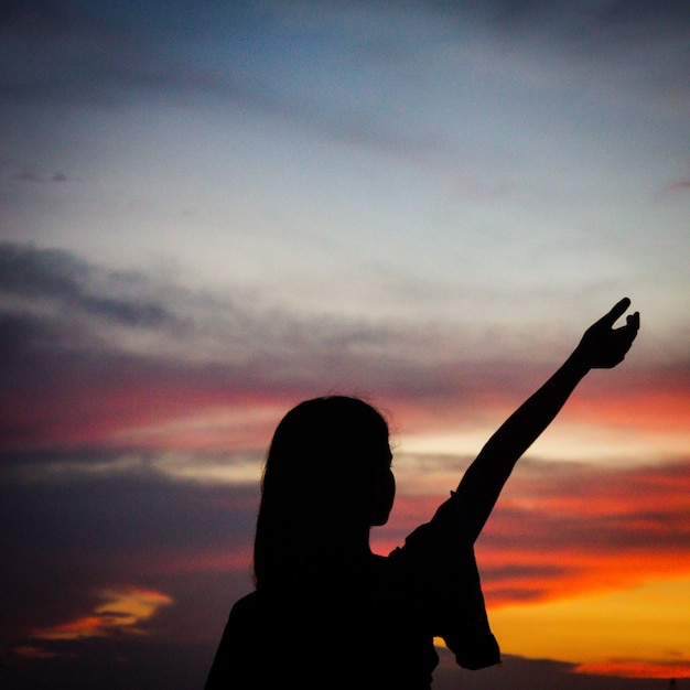 Foto silhouette di donna con le braccia alzate contro il cielo durante il tramonto