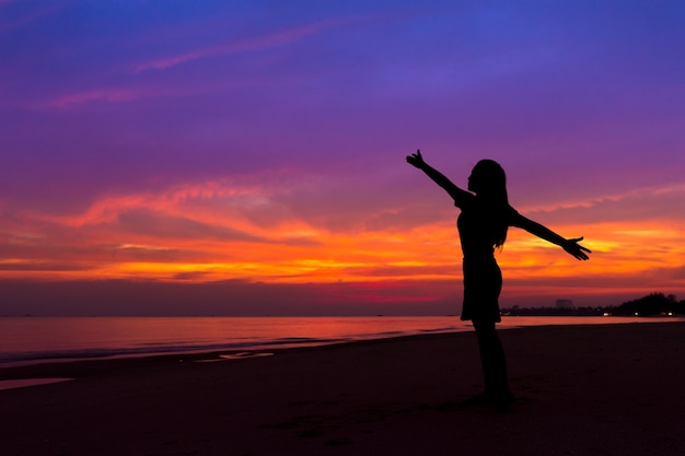 Siluetta della donna con le mani su mentre stando sulla spiaggia del mare al tramonto