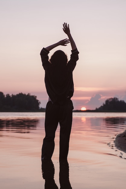 Silhouette of woman with her hands raised young slender brunette with long brown hair in black suit ...