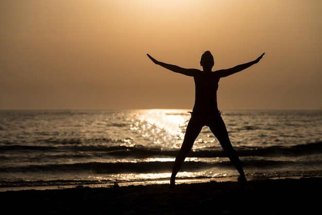 Silhouette di donna con le mani alzate e saltare sulla spiaggia al tramonto copia spazio testo