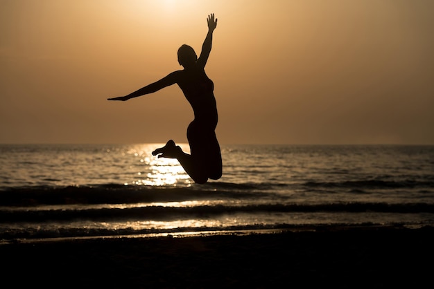 Silhouette di donna con le mani alzate e saltare sulla spiaggia al tramonto copia spazio testo