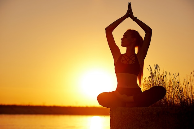 Silhouette woman with yoga posture on the beach pier at sunset or sunrise