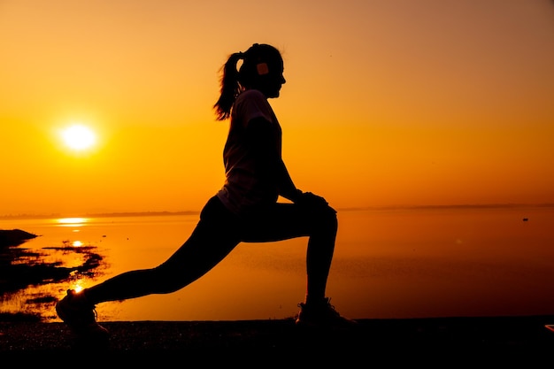 Тренировка женщины силуэта в одиночку с фоном заката. Здоровая и сольная физическая активность. Оздоровительный образ жизни и отдых на природе.