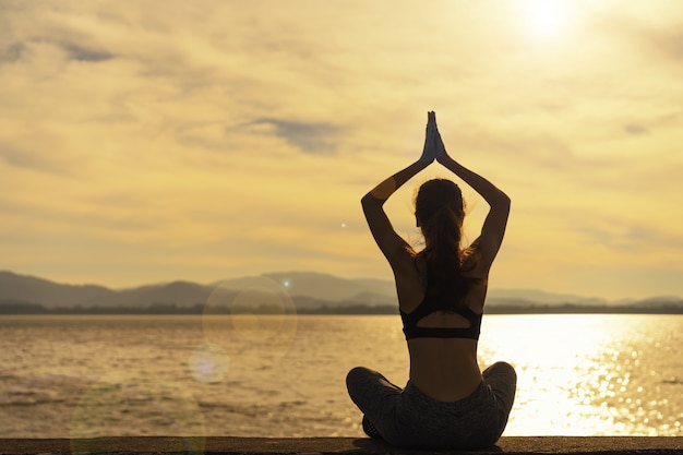 Silhouette le donne praticano yoga al mattino presso il bacino idrico.