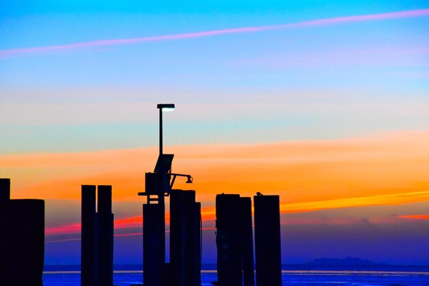 Silhouette wooden post by sea against sky during sunset