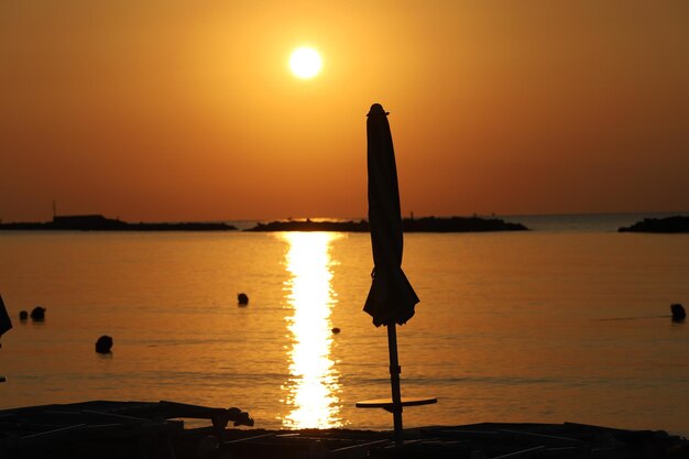 Silhouette wooden post in sea against sky during sunset