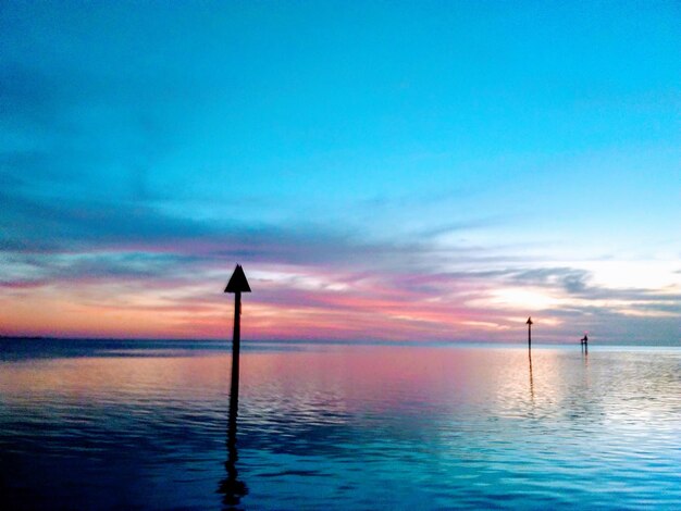 Silhouette wooden post in sea against sky during sunset