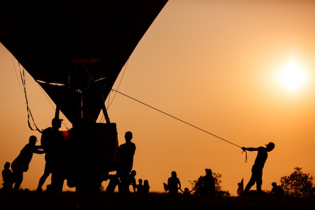 silhouette of worker drag hot air balloon basket in sunset