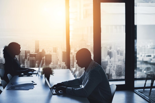 Photo silhouette working and sitting in the city office to focus in the morning business people and typing at the boardroom table at a calm time of day cityscape window and flare view of urban life