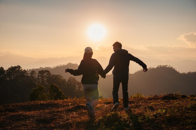 Silhouette young asian couple holding hands enjoying on hill in countryside at sunset