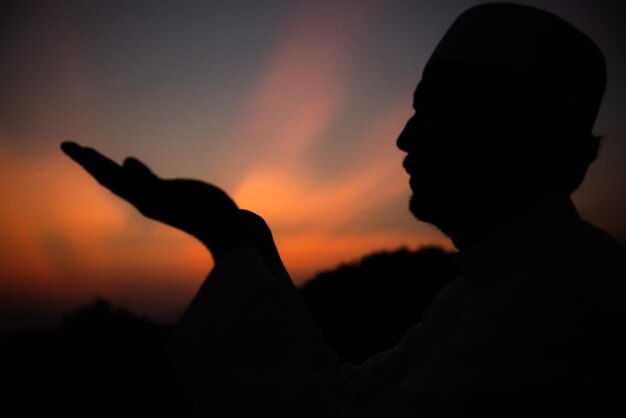 シルエット若いアジアのイスラム教徒の男性が日没で祈るラマダン祭のコンセプト