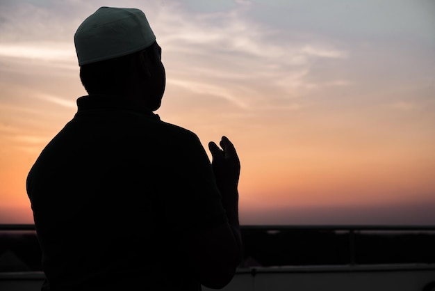 シルエット若いアジアのイスラム教徒の男性が日没で祈るラマダン祭のコンセプト