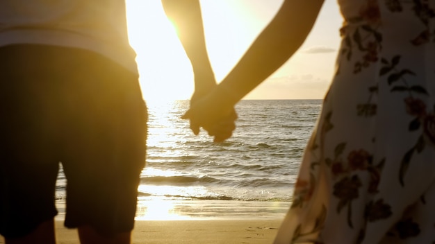 Silhouette of young family running joining hands on beach to boundless ocean against sunset on horizon backside view