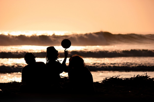 Photo silhouette of young friends playing with a ball on the beach on sunset