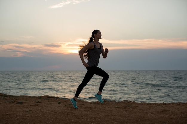 Siluetta di una giovane ragazza che corre lungo la spiaggia del mare durante un tramonto incredibile