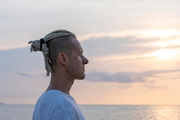 Silhouette of a young guy with dreadlocks on his head near sea during sunset Close up portrait