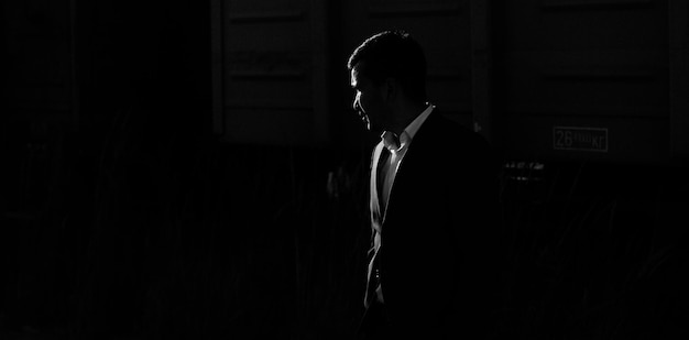 Photo silhouette of young man in the classic suit looking away with harsh backlighting