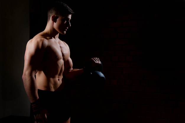 Silhouette of a young man doing weight exercises with a dumbbell