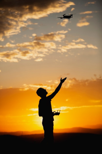 Silhouette of a young man operating a drone in A Rural Setting on sunset