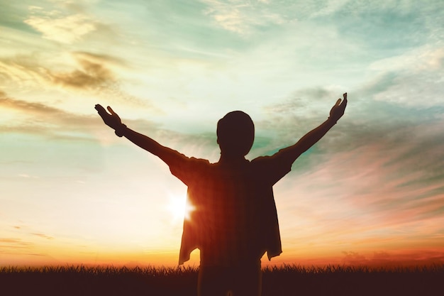 Silhouette of young man raising hands at park