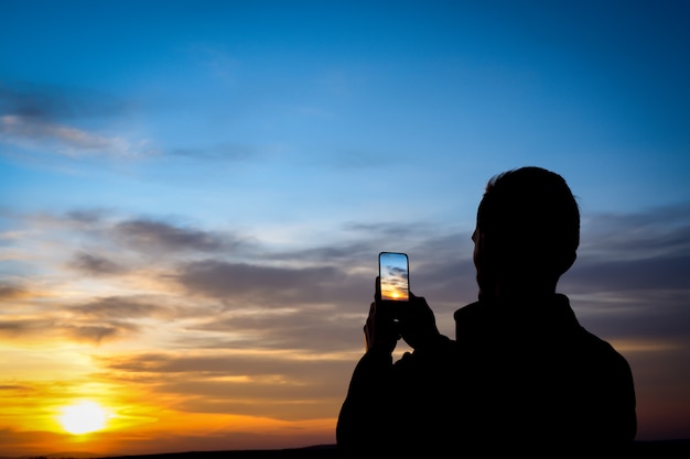 Silhouette of young man shoots sunset on phone, smartphone. Travel, walking.