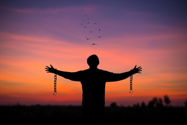 Silhouette of young man standing alone with beautiful sky at sunset open both arms with chains on his arms He felt free from the shackles tied to his arms