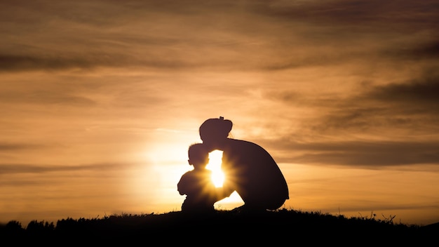 Silhouette of a young mother lovingly kissing her little child on the sunset