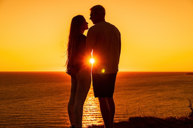 빨간색으로 바다 위의 절벽에서 저녁을 즐기는 젊은 로맨틱 커플의 실루엣