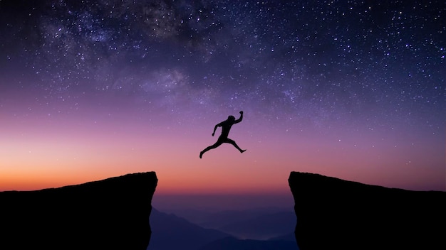 Silhouette of young traveler and backpacker jumping on cliff at night with the star and milky way over the sky He enjoyed traveling and was successful when he reached the summit