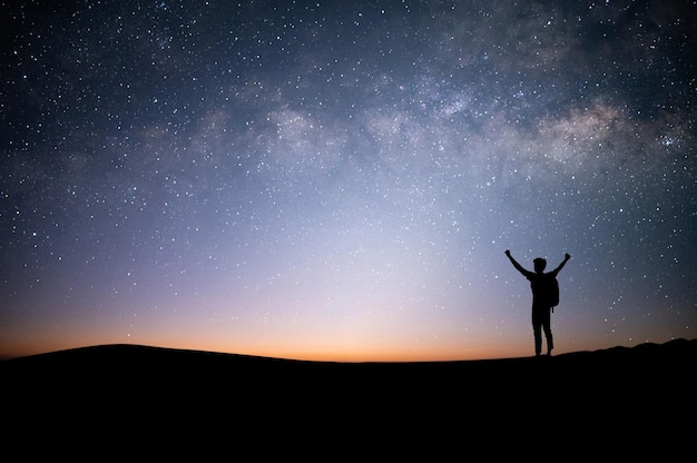 Silhouette of young traveler standing and open both arm watched\
night sky view star and milky way alone on top of the mountain he\
enjoyed traveling and was successful when he reached the\
summit