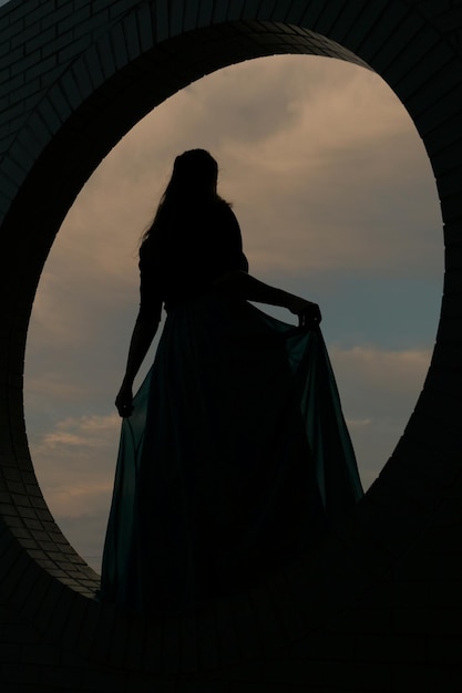 Silhouette of young woman in a blue dress against a clouded sky