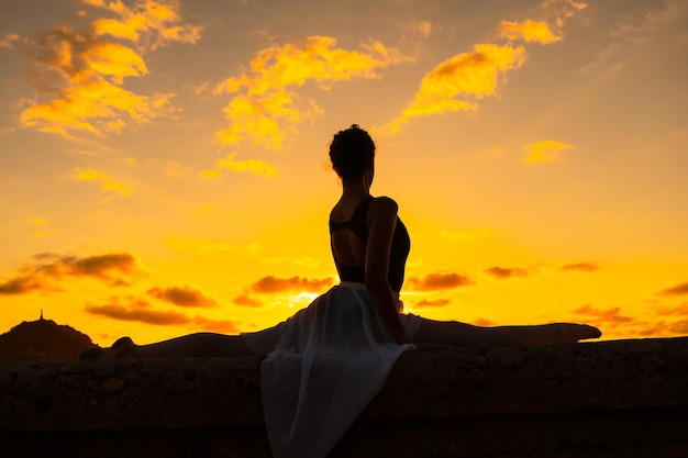 Silhouette of a young woman dancer by the beach at sunset doing spagata