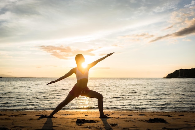 silhouette young woman exercising at beach against sky during sunset