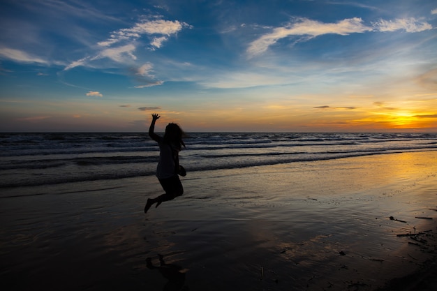 Silhouette of a young woman flying in the sky at sunset on the sea.