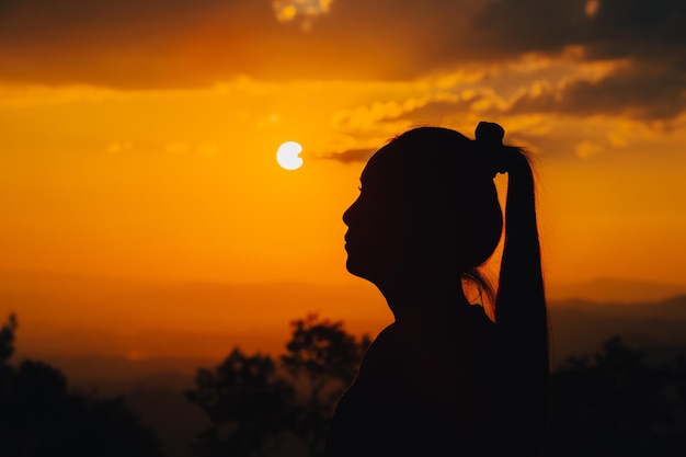 シルエットの若い女性が夕日を見ています。