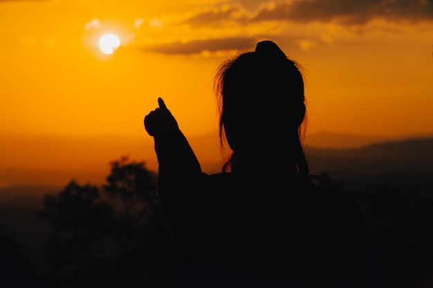 Photo silhouette young woman is pointing at the sunset.