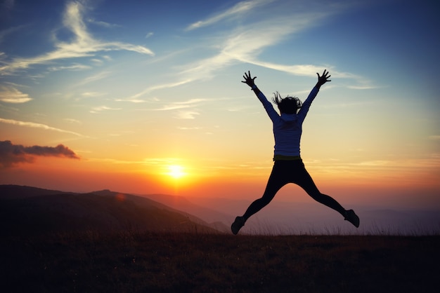 Photo silhouette of young woman jumping against sunset with blue sky.