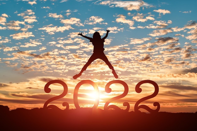 Silhouette of young woman jumping to Happy new year 2022 in sunset or sunrise background.