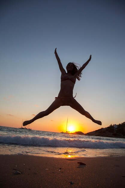 Silhouette of a young woman jumping  with legs and arms open in a beach