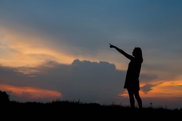 Silhouette young woman pointing forward to Dream ahead in sunset sky