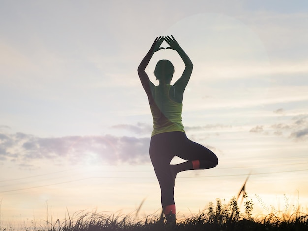 Silhouette young woman practicing yoga at backyard