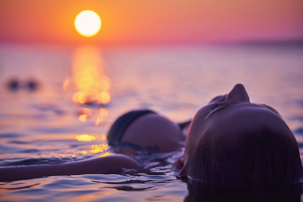 日の出のビーチでヨガを練習する若い女性のシルエット