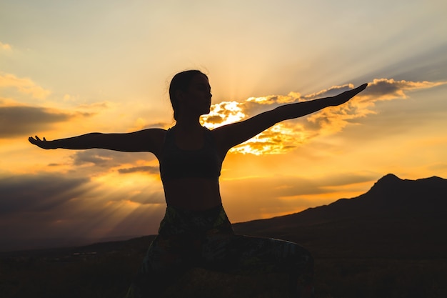 Siluetta di yoga di pratica della giovane donna al tramonto