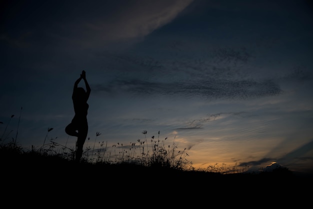 日没時にヨガを練習している若い女性のシルエット