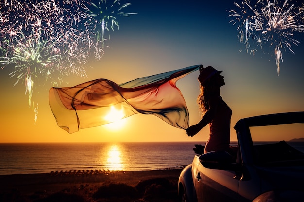 silhouette of young woman relaxing at the beach fireworks in sunset sky summer vacation concept