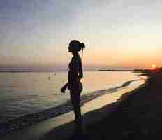 Photo silhouette young woman standing on beach against sky during sunset