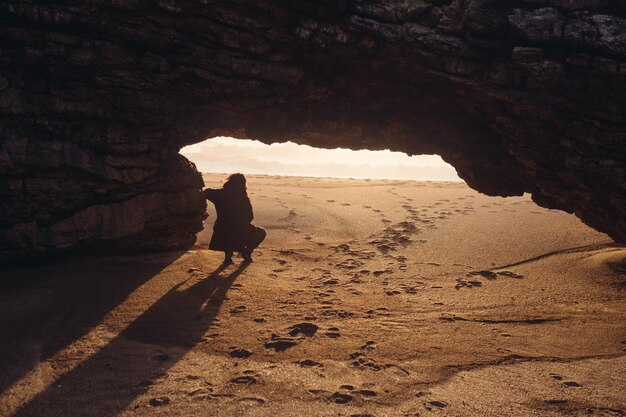 사진 해가 지는 동안 해변 에 있는 바위 형성 에 서 있는 젊은 여자 의 실루